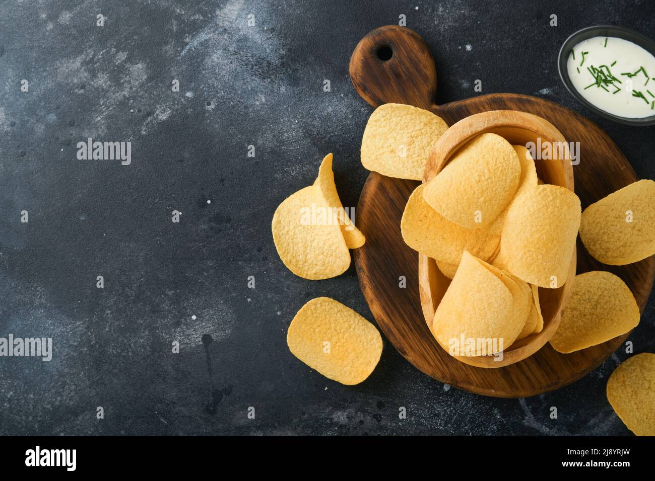 Cibo malsano. Spuntini. Tutti i classici spuntini di patate con arachidi, anelli di popcorn e cipolle e pretzel salati in ciotole su backgroun di cemento nero Foto Stock