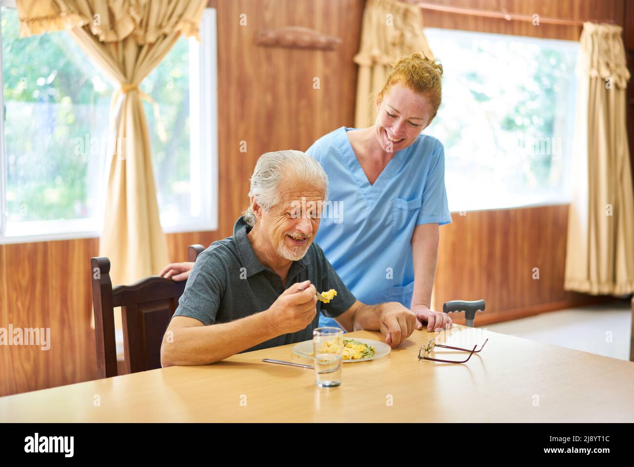 Un caregiver cordiale o un infermiere geriatrico assiste gli anziani a pranzo in una vita assistita Foto Stock