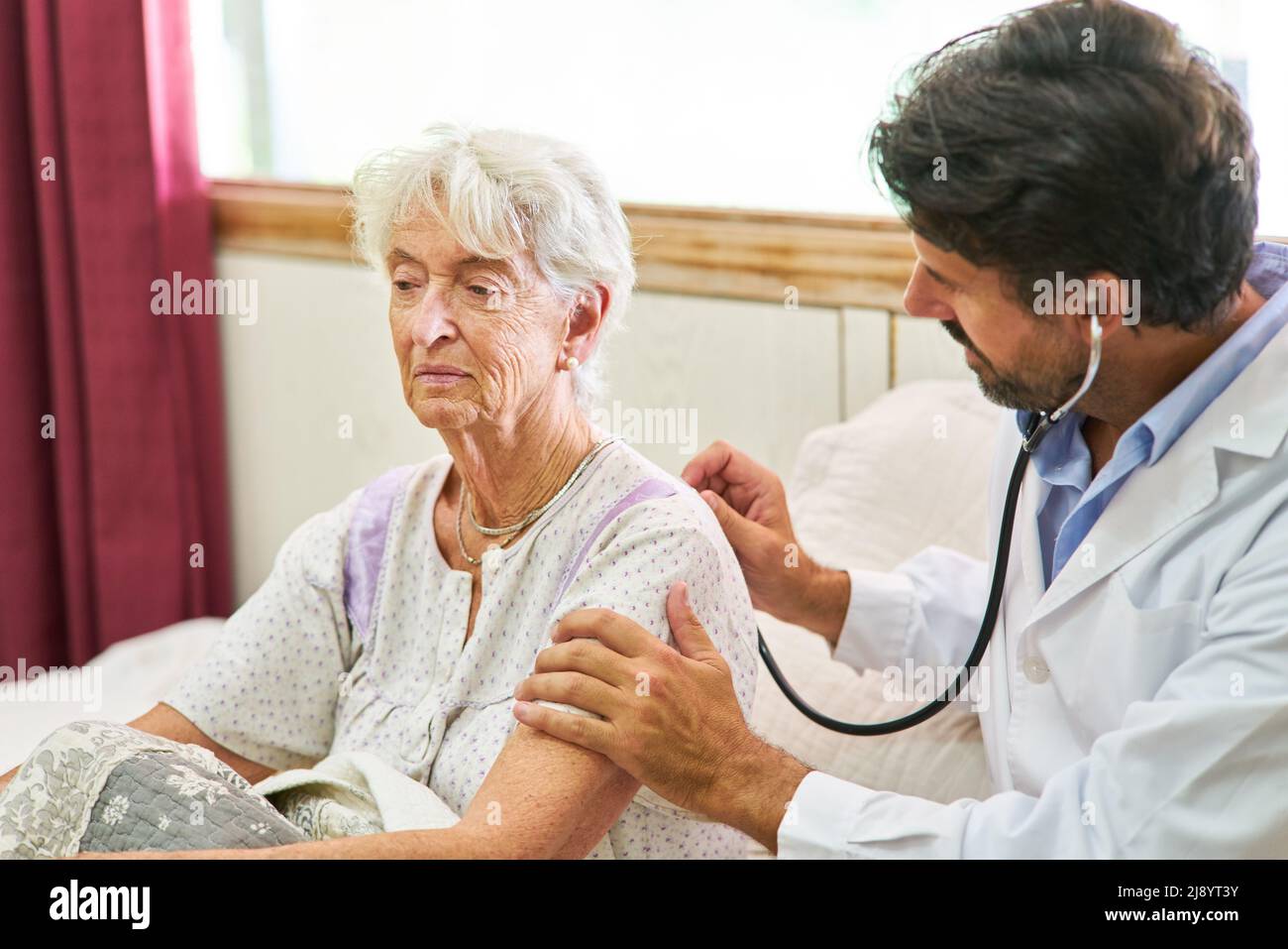 Donna anziana malata a letto che è esaminata con stetoscopio dal medico durante la visita domestica Foto Stock