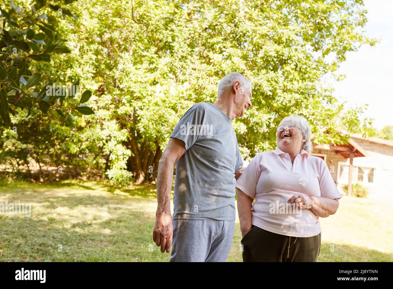 Una coppia in pensione ride allegro a una battuta durante una passeggiata nel parco in estate Foto Stock