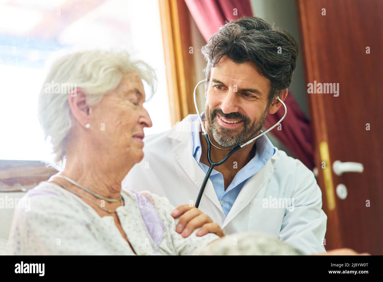 Medico generico che ascolta una donna anziana malata con uno stetoscopio durante una visita a casa Foto Stock