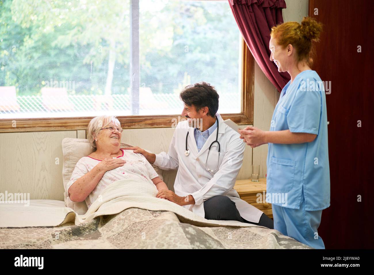 Il medico siede al letto della donna anziana malata come paziente nella casa di cura o nell'assistenza domestica Foto Stock