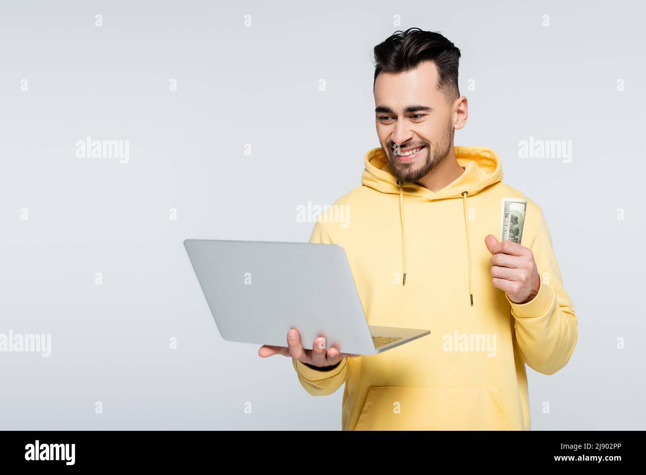 felice giocatore che detiene dollari e laptop isolato su grigio Foto Stock