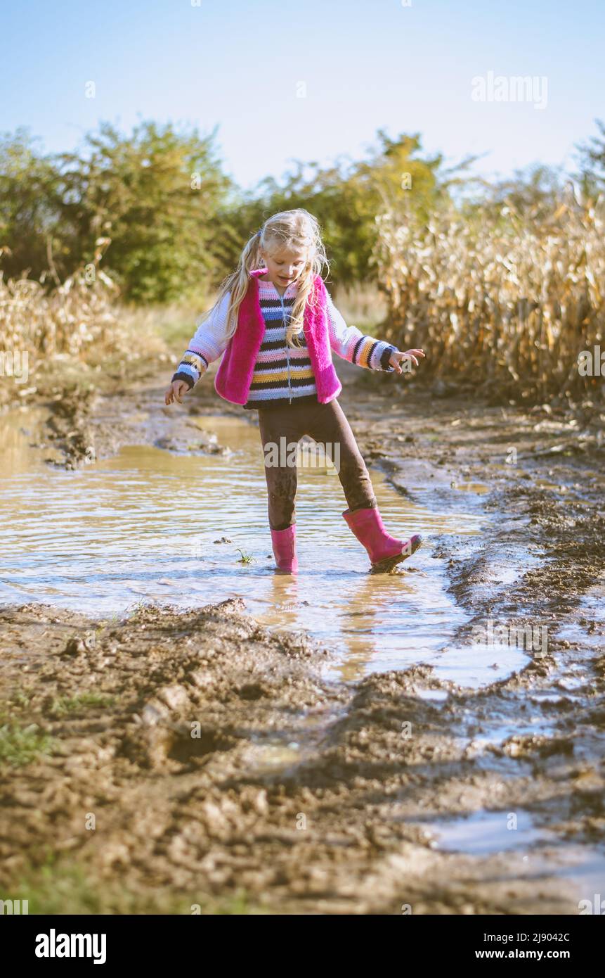 piccola ragazza bella godendo pozza d'acqua dopo la pioggia in stagione autunnale soleggiato atmosfera Foto Stock