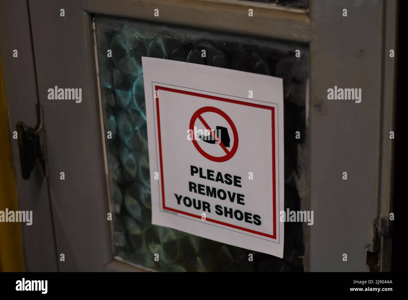 Avviso "rimuovere le scarpe" su una porta Foto Stock