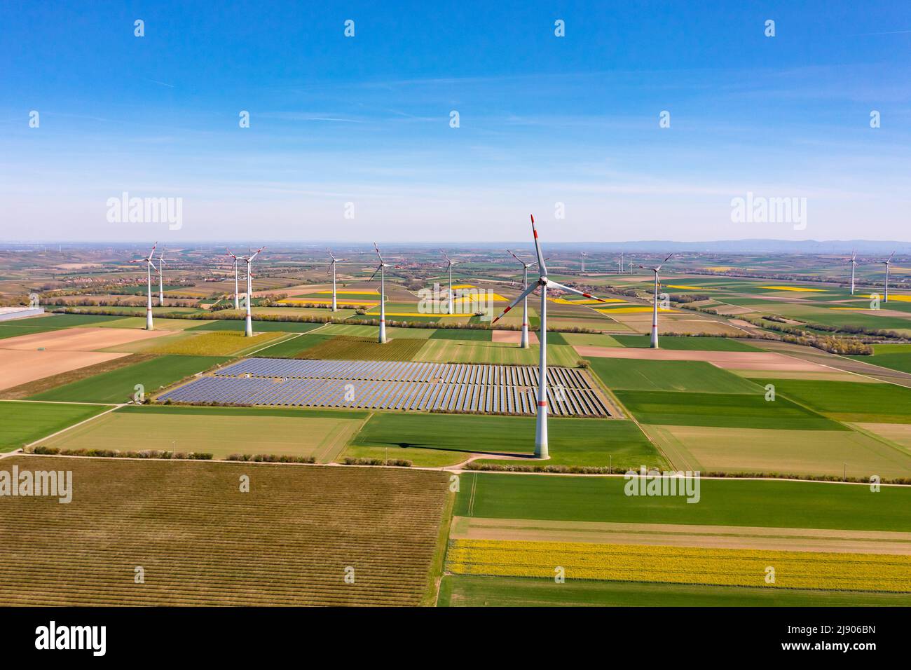 Produzione di energia elettrica con turbine eoliche e parco solare tra campi da una prospettiva drone Foto Stock