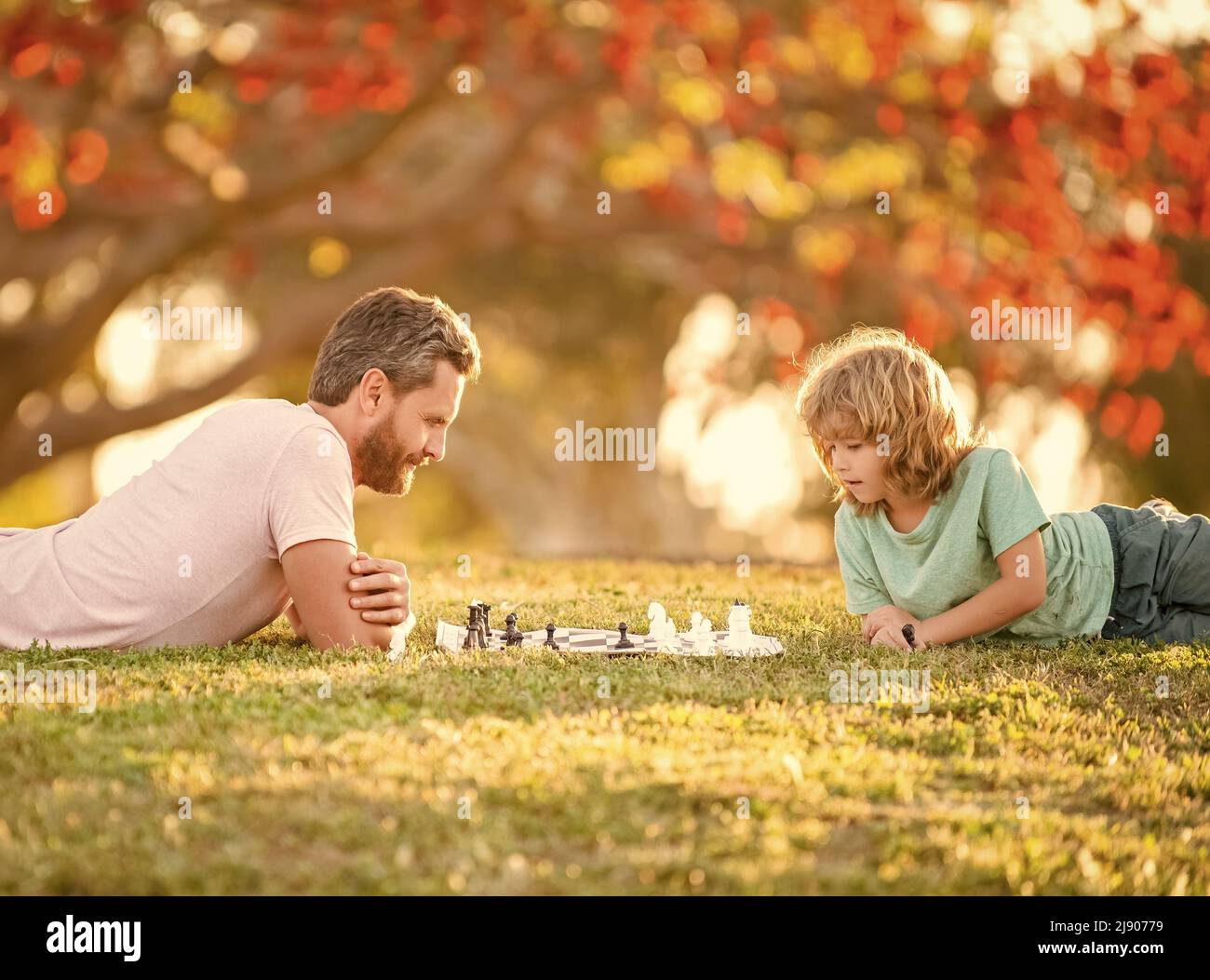 famiglia felice di papà e figlio capretto che gioca a scacchi su erba verde nel parco all'aperto, genio Foto Stock