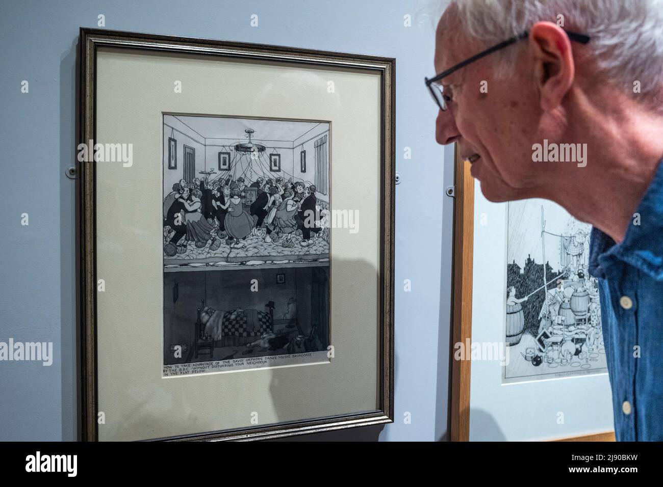 Londra, Regno Unito. 19 maggio 2022. Geoffrey Beare, curatore, vede 'come trarre vantaggio dalla musica dance dei Savoy Orpheans trasmessa dalla BBC senza disturbare il vostro vicino nell'appartamento sottostante', 1928, Di William Heath Robinson in anteprima di una nuova mostra “The Humor of William Heath Robinson” al museo Heath Robinson di Pinner, a nord-ovest di Londra. Il suo nome entrò nella lingua già nel 1912 ed è ancora in uso quotidiano per descrivere il tipo di contrapposizioni ad hoc che compariva in molti dei suoi cartoni animati. La mostra, che si svolge dal 21 maggio al 4 settembre 2022, celebra l’opera dell’artista Foto Stock