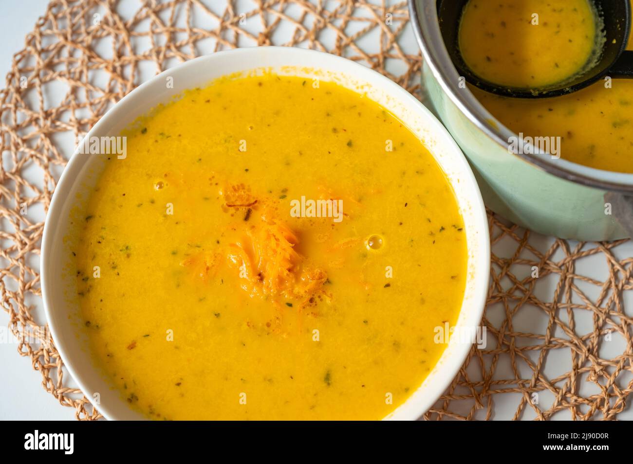Zuppa di carote cremosa in piatto e in pentola su tampone di bambù su tavola bianca, primo piano. Foto Stock