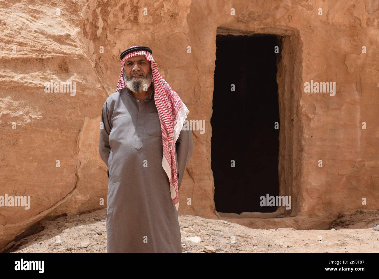 Un uomo arabo locale che indossa il keffiyeh in piedi di fronte ad una porta scolpita nel deserto Rick preteso essere la Grotta di Alibaba Foto Stock