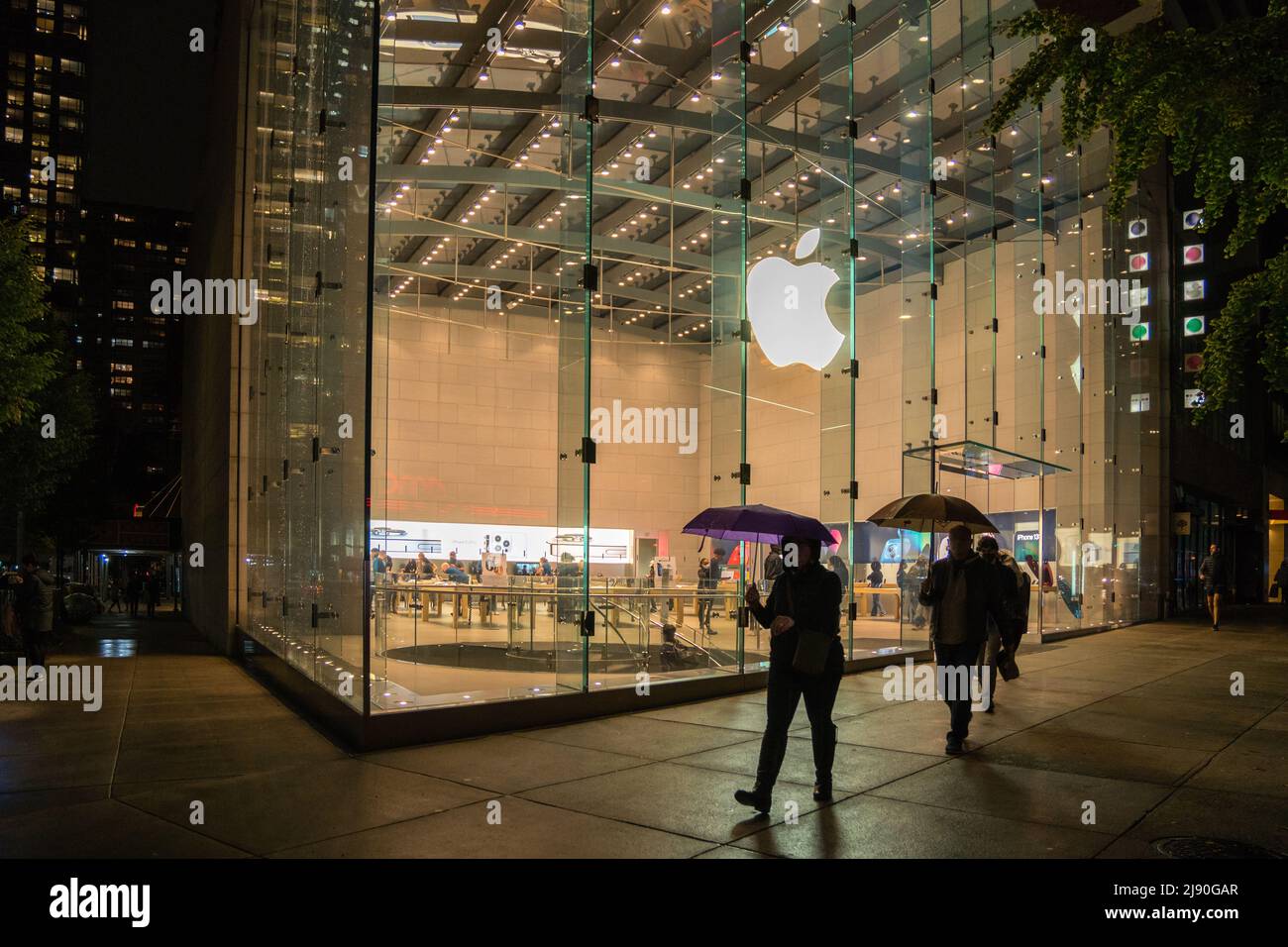 New York, NY, US-Ottobre 26, 2021: Persone con ombrelloni camminano presso Apple computer Store in una notte di pioggia. Foto Stock