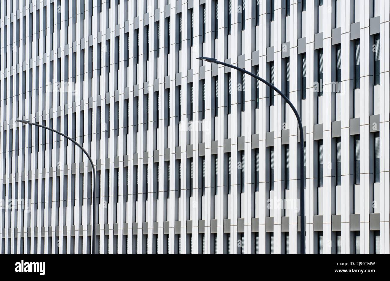 Modello di linea di architettura geometrica. La perfetta simmetria della facciata di un edificio di uffici interrotto dalle linee curve di due lampioni Foto Stock