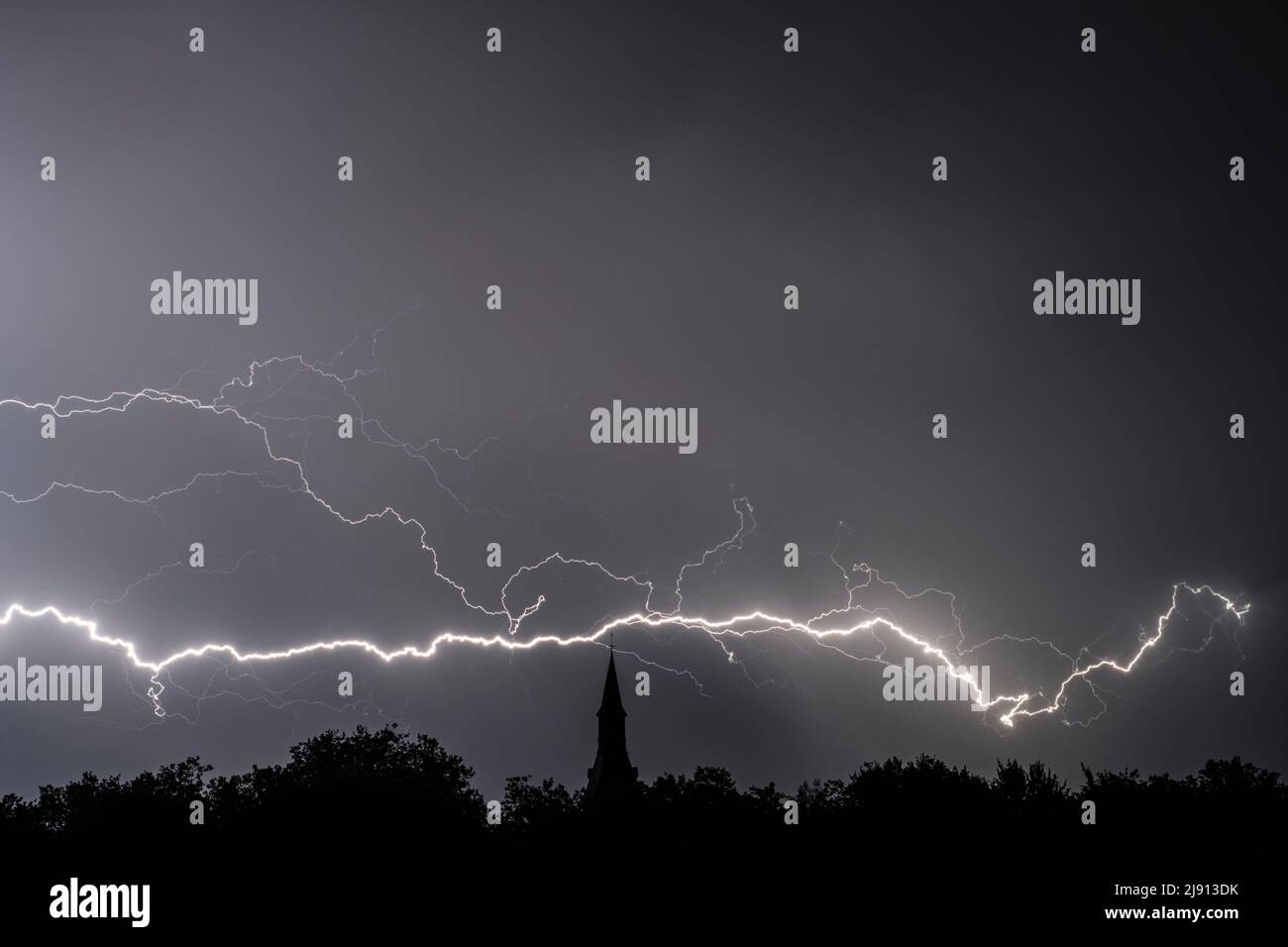 Pioggia caduta e colpo di fulmine a forcella durante la tempesta di notte sopra la torre della chiesa e gli alberi Foto Stock