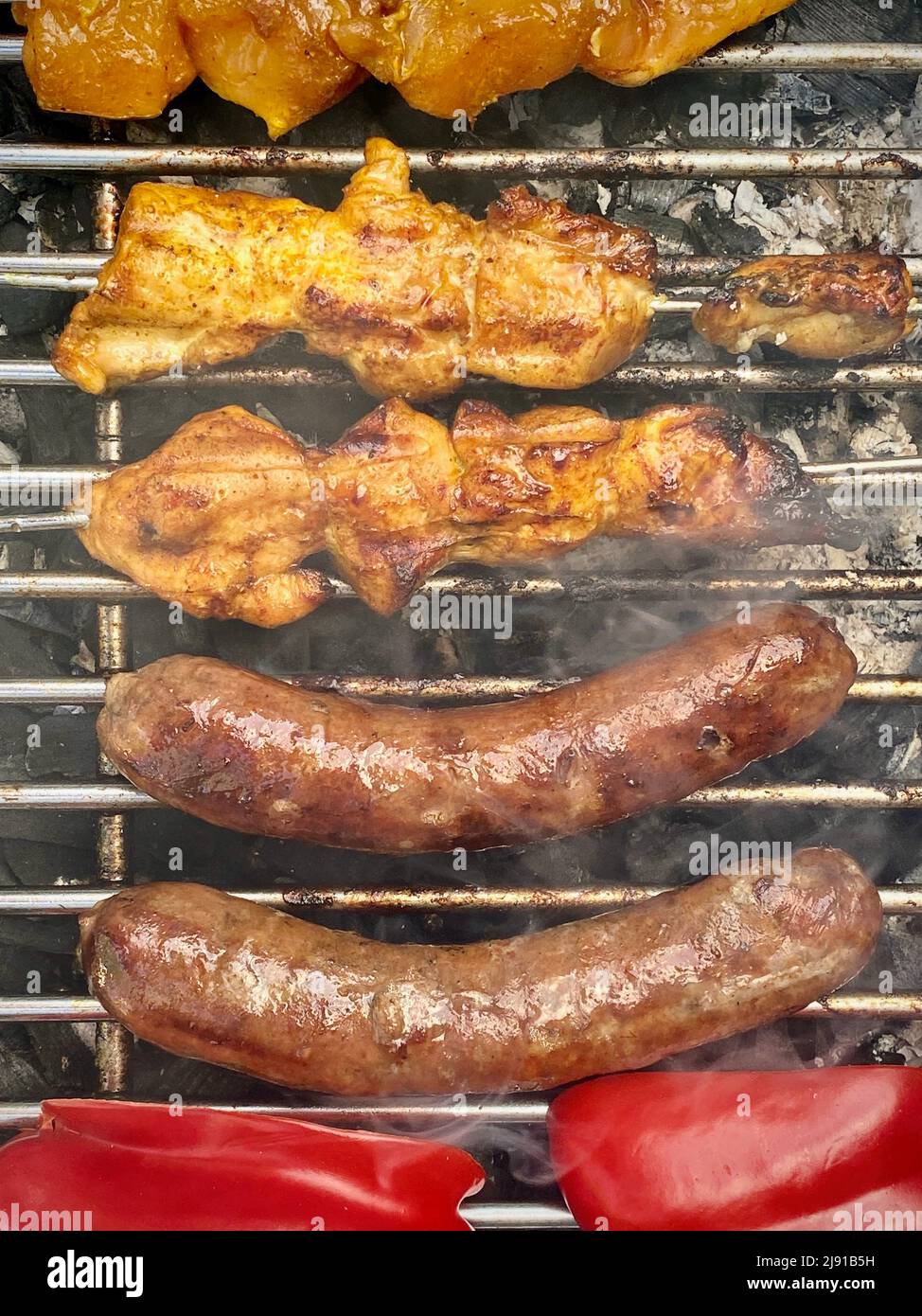 Barbecue barbecue di salsicce grigliate affumicate, satay di carne sui bastoni e peperoni rossi tagliati che cucinano il cibo all'aperto su salumi caldi. Concetto di cibo. Foto Stock