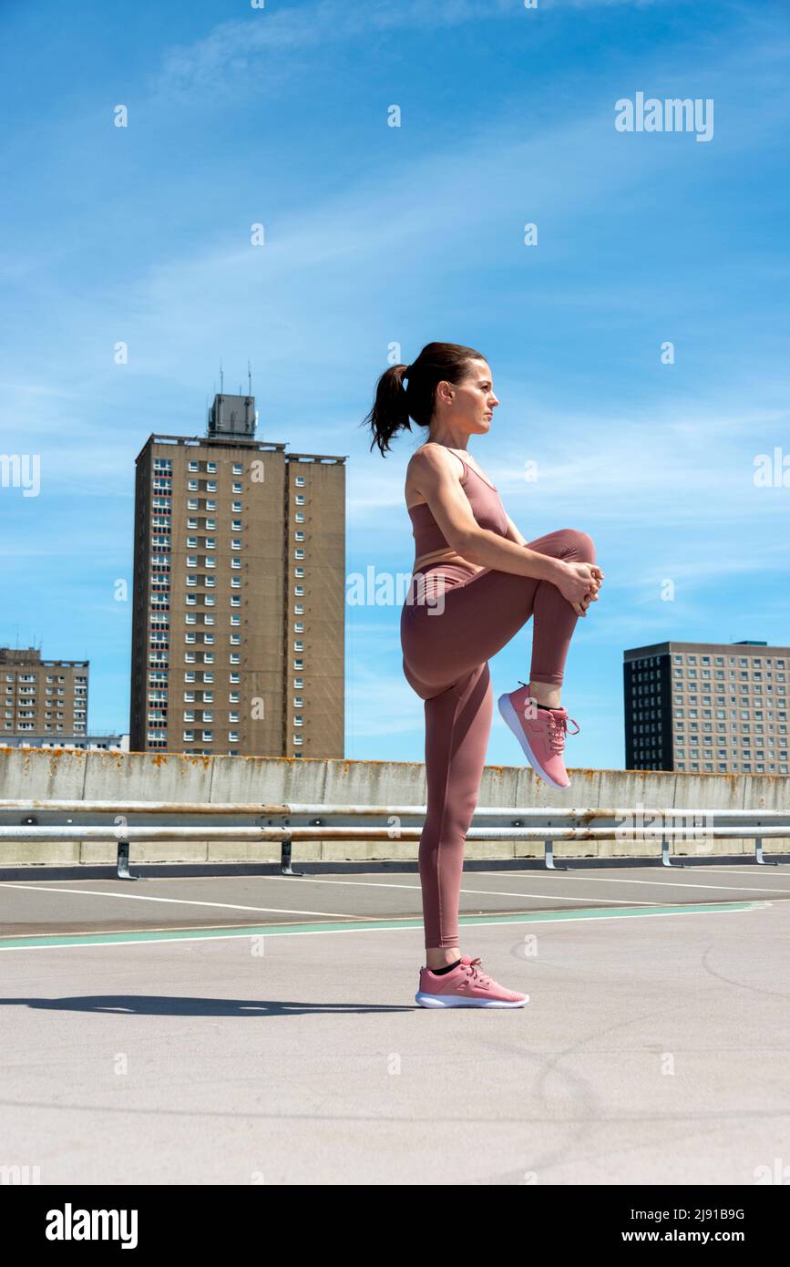 Donna sportiva che fa una gamba stretch riscaldamento esercizio fuori, ambiente urbano. Foto Stock
