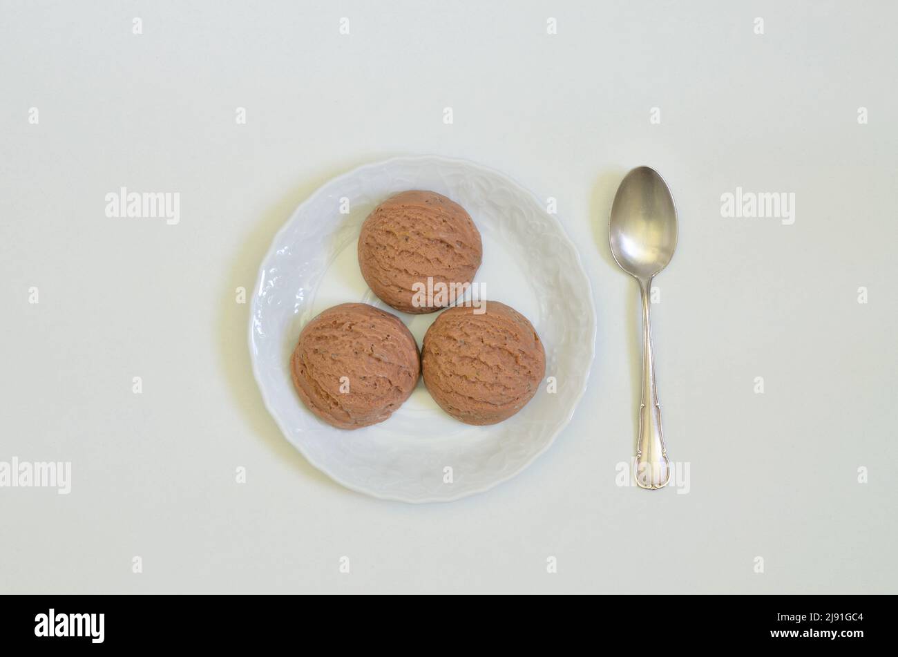 vista dall'alto di tre cucchiai di gelato al cioccolato su piatto bianco con cucchiaio, sfondo bianco con spazio per il testo Foto Stock