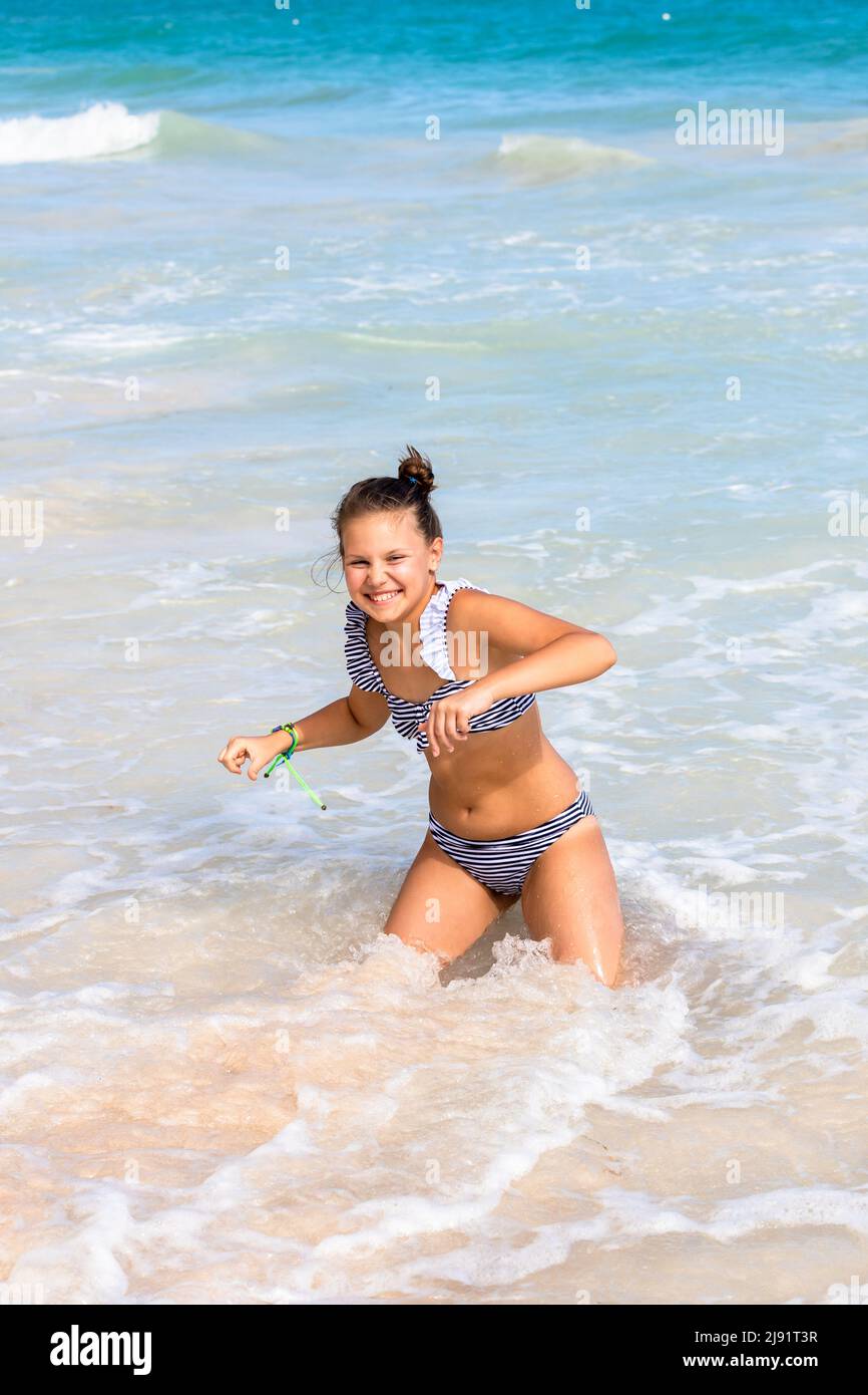 La ragazza piccola felice in costume da bagno è in un'acqua di riva. Foto all'aperto scattata alla spiaggia di Bavaro, Repubblica Dominicana, in una giornata di sole Foto Stock