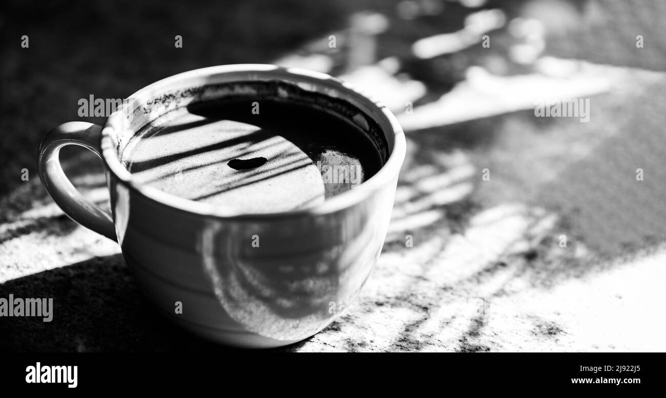 Una tazza di caffè. I raggi del sole del mattino brillano su una tazza di caffè nero con schiuma. Una bevanda stimolante con caffeina. Foto Stock