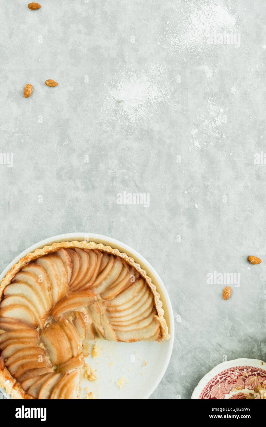 Crostata di pera su sfondo di marmo grigio con mandorle sparse, zucchero e cannella per un dessert autunnale Foto Stock