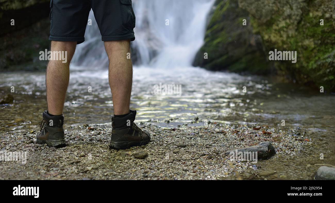 uomo in scarponi da trekking in piedi da una cascata Foto Stock
