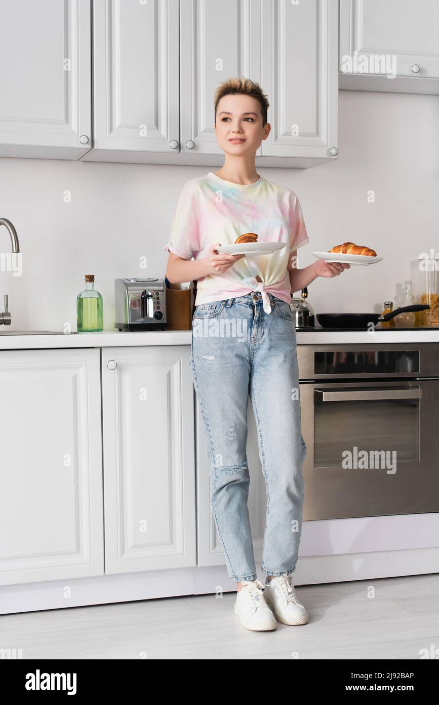 intera lunghezza di pangender positivo persona in jeans che tiene gustosi  croissant in cucina Foto stock - Alamy