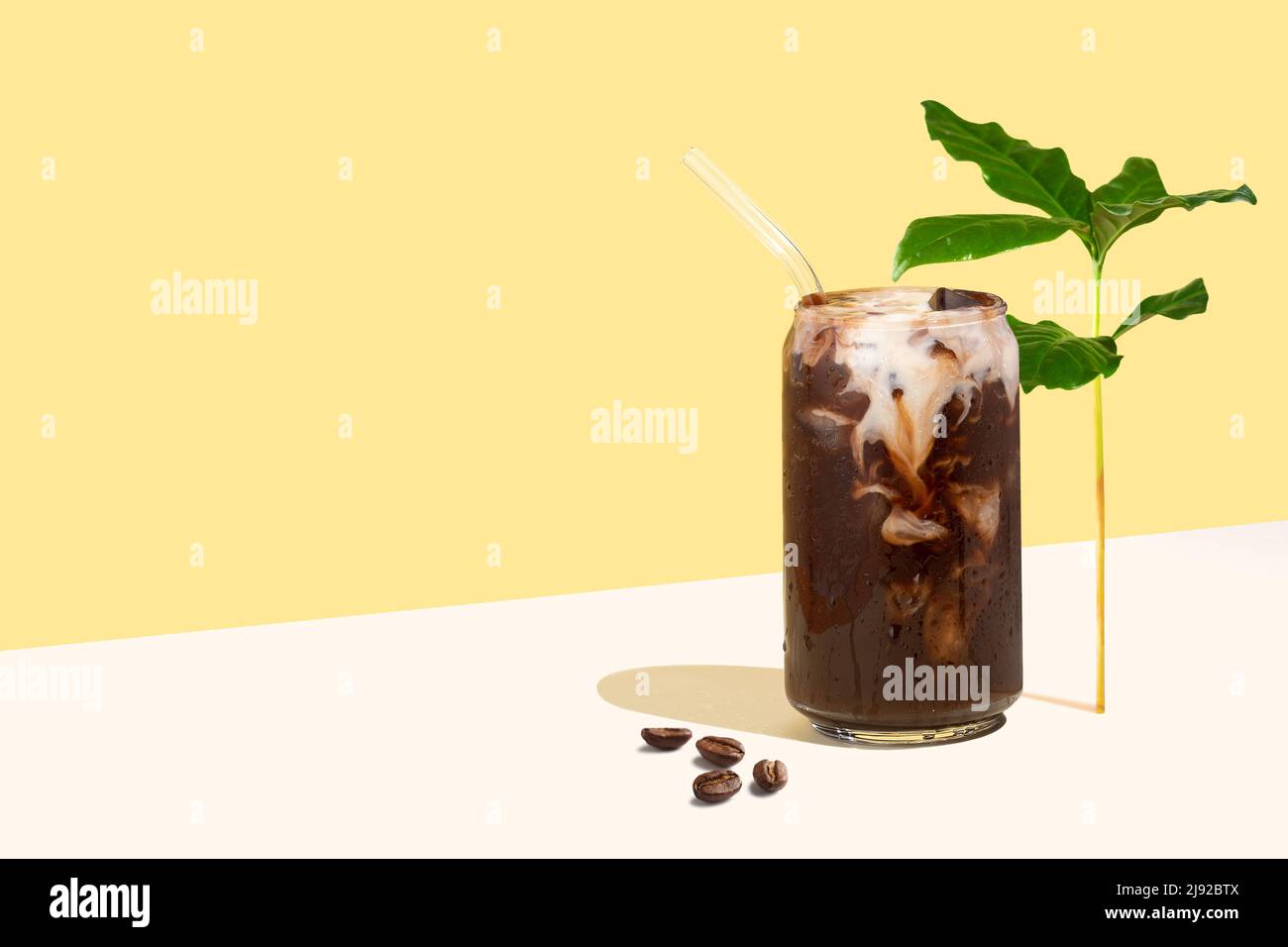 Bevanda fredda di caffè, chicchi di caffè e foglie su sfondo di proiezione diagonale isometrica giallo. Tazza di caffè in vetro a forma di lattina con latte vegetale. Foto Stock