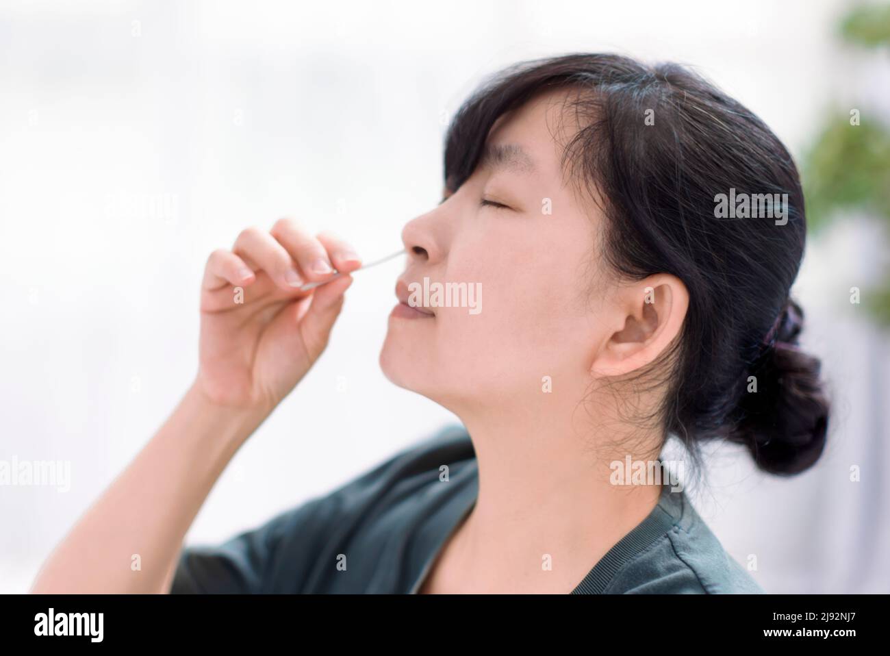 Donna che usa il kit auto-test dell'antigene rapido covid-19 a casa con un tampone nasale di cotone Foto Stock