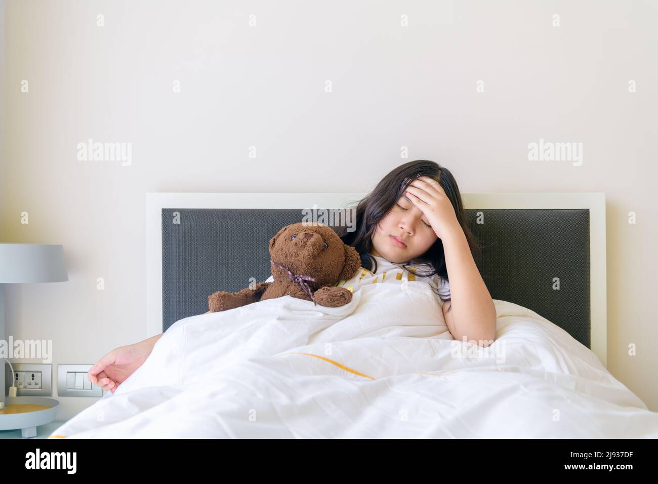 Bambino asiatico carino o ragazza capretto mal di testa mal di testa malati e mano alla fronte con triste a letto, concetto di assistenza sanitaria Foto Stock