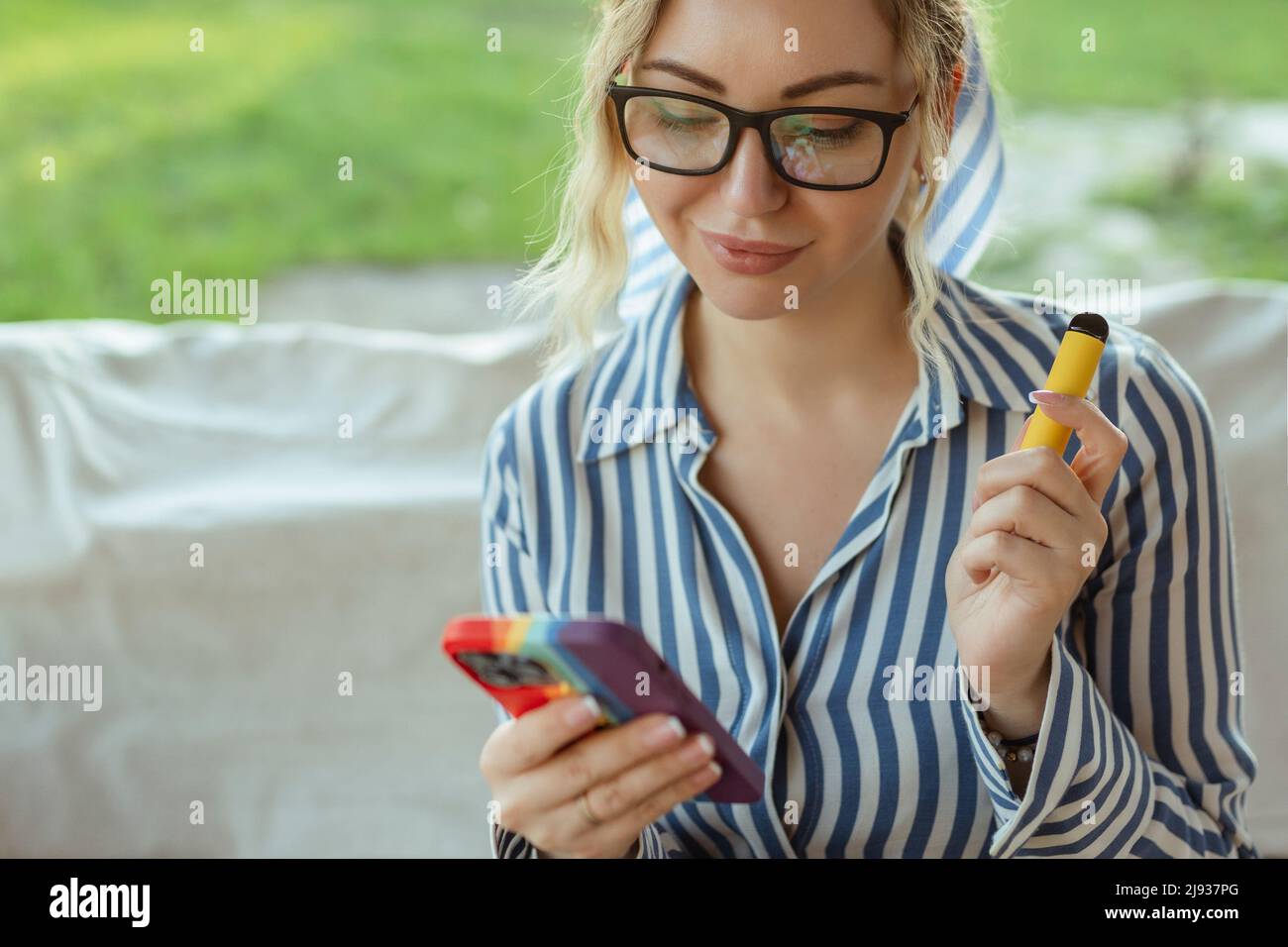 Bella donna fumare e-sigaretta per strada e utilizzare smartphone . Foto Stock