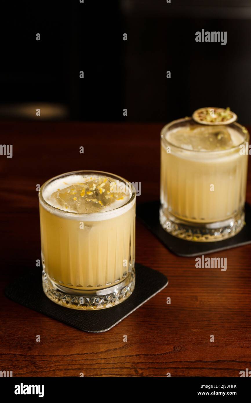 Cocktail dai colori caldi. Cocktail mezcal e cocktail alcolico Scotch Whiskey Penicillin drink. Bicchiere da cocktail sul banco del bar. Foto Stock