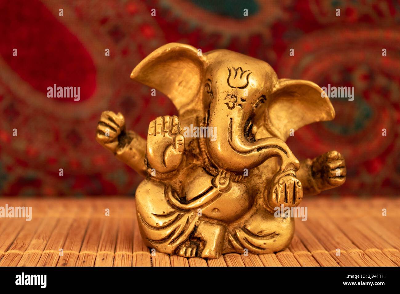 Scultura ganesha d'oro su tappeto di legno con sfondo paisley, primo piano. Concetto di meditazione Foto Stock