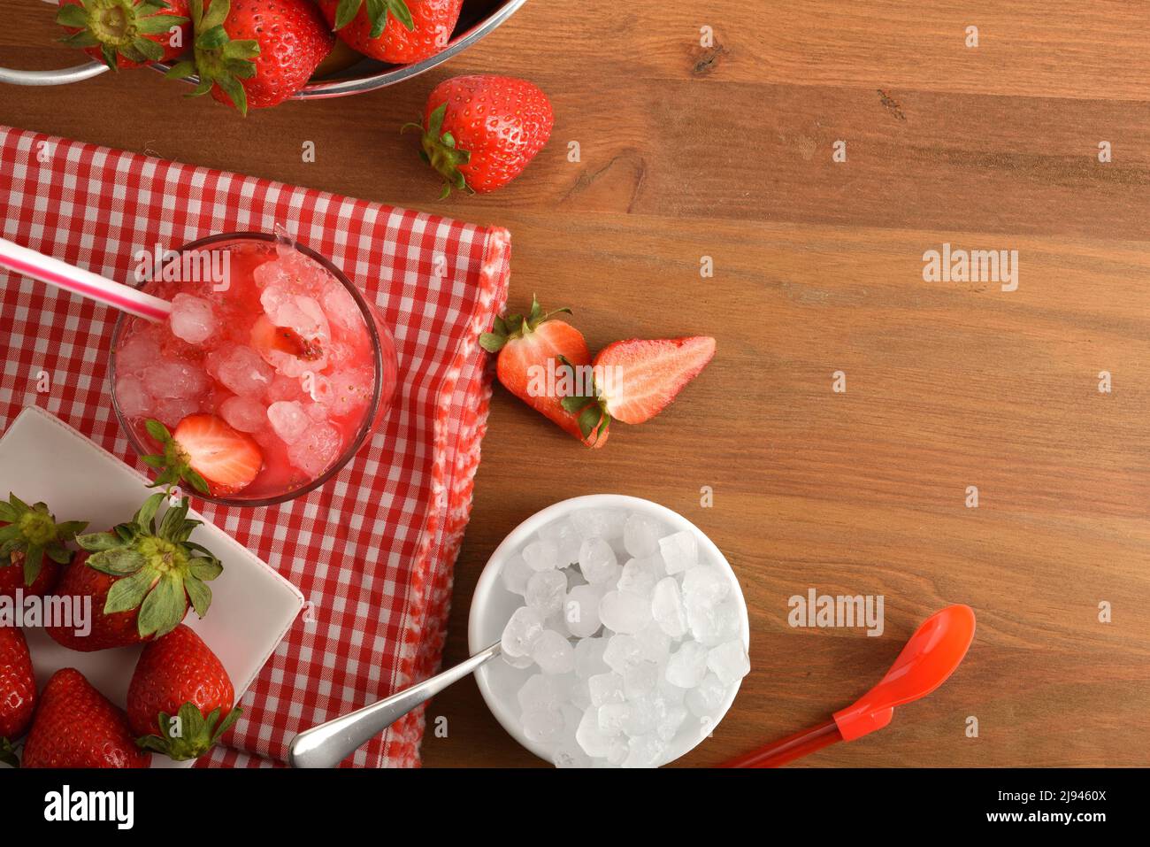 Granita di frutta con fragole mature con molto ghiaccio su tavola di legno con ciotola con ghiaccio e cestino pieno di fragole. Vista dall'alto. Composizione orizzontale Foto Stock