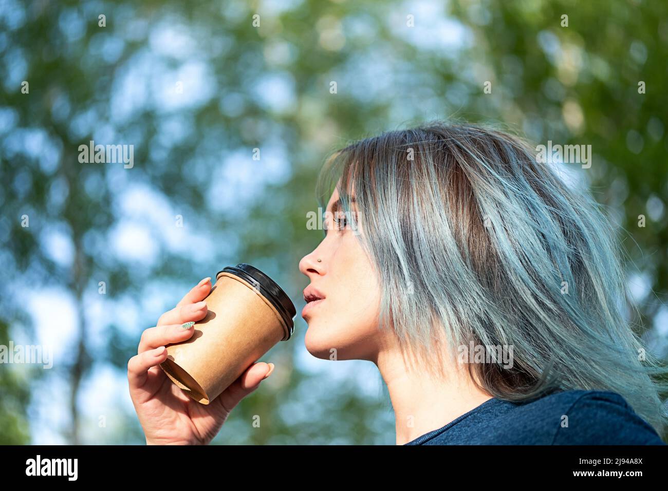 Le bevande della donna dai capelli blu take away il caffè all'aperto sullo sfondo della natura. Foto Stock