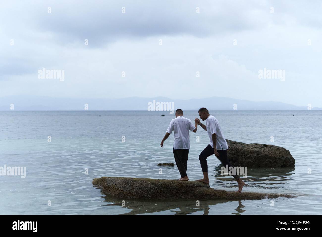 Coppia gay che saltano tra le rocce in mezzo al mare durante il crepuscolo Foto Stock