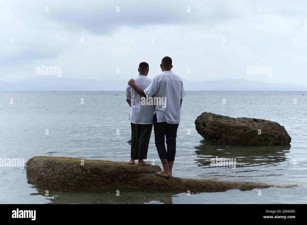 Parte posteriore di una coppia gay in piedi su una roccia che guarda all'orizzonte dell'oceano Foto Stock