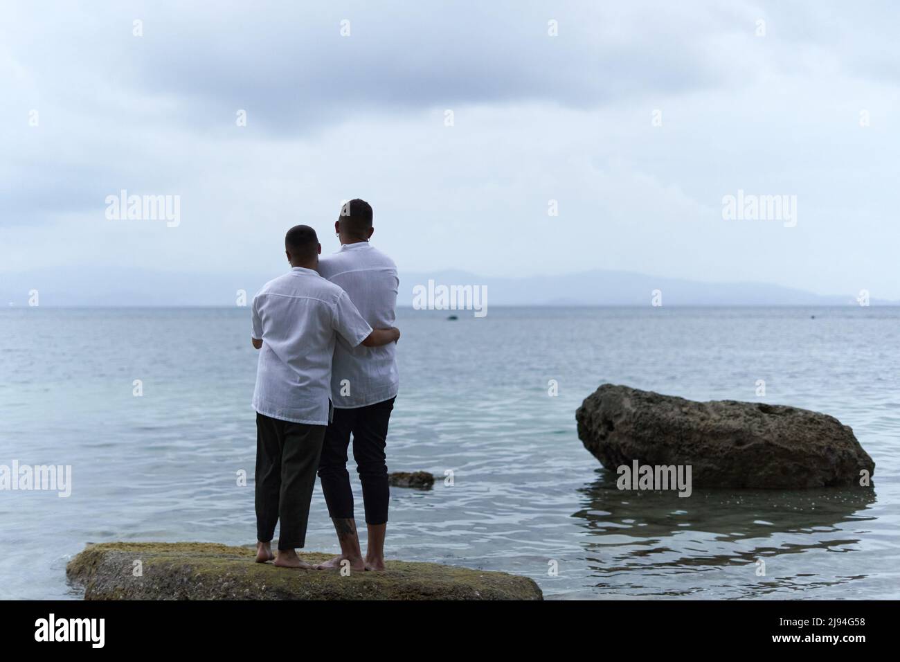 Parte posteriore di una coppia omosessuale in piedi su una roccia che guarda l'orizzonte dell'oceano Foto Stock