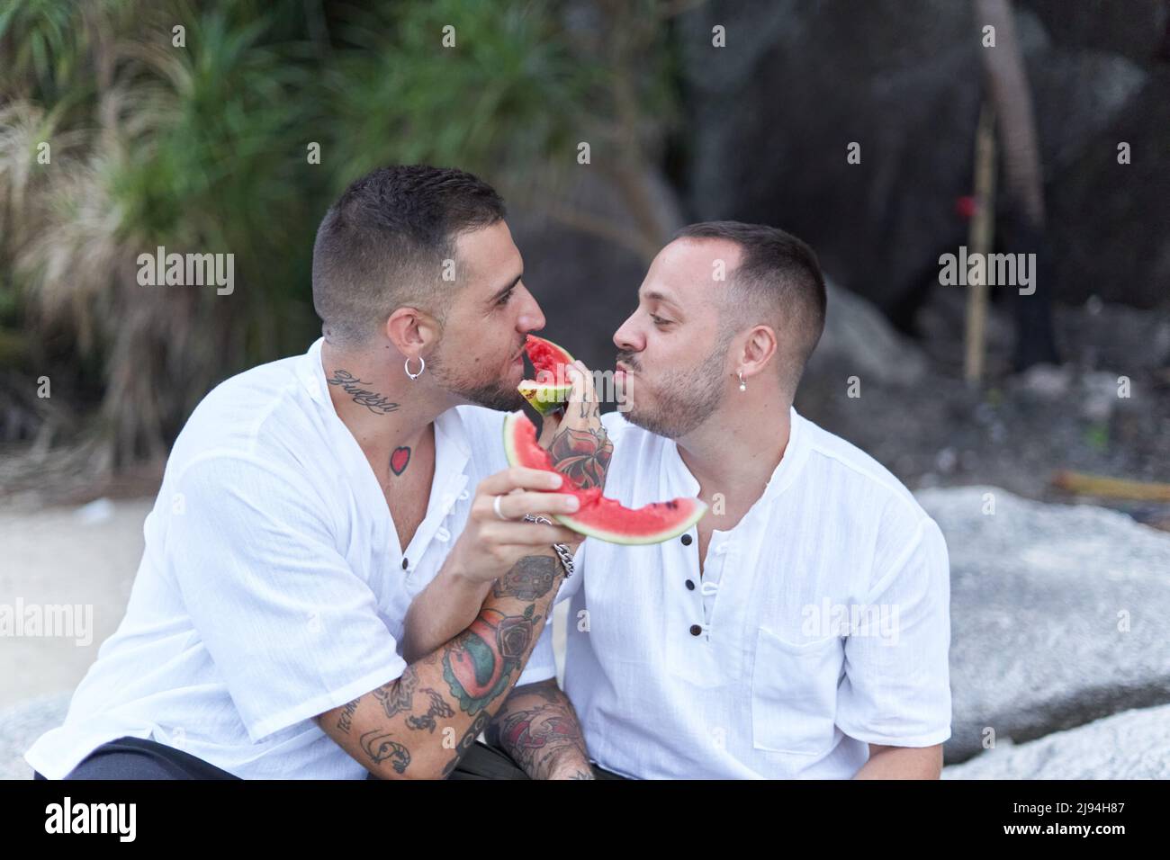 Coppia gay scherzando mentre si nutrono l'un l'altro con l'anguria all'aperto Foto Stock