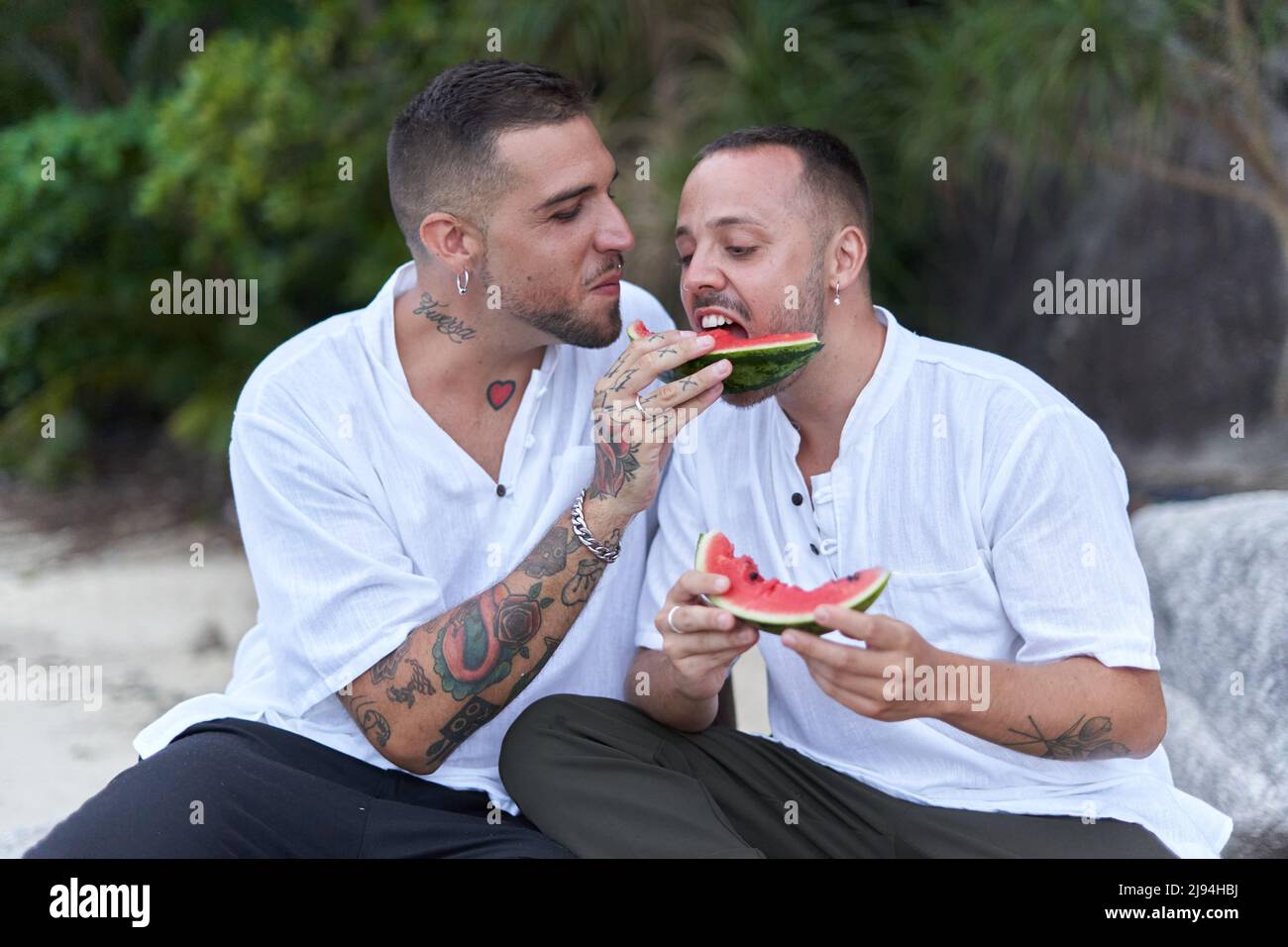 coppia gay che condivide una fetta di cocomero su una spiaggia tropicale Foto Stock
