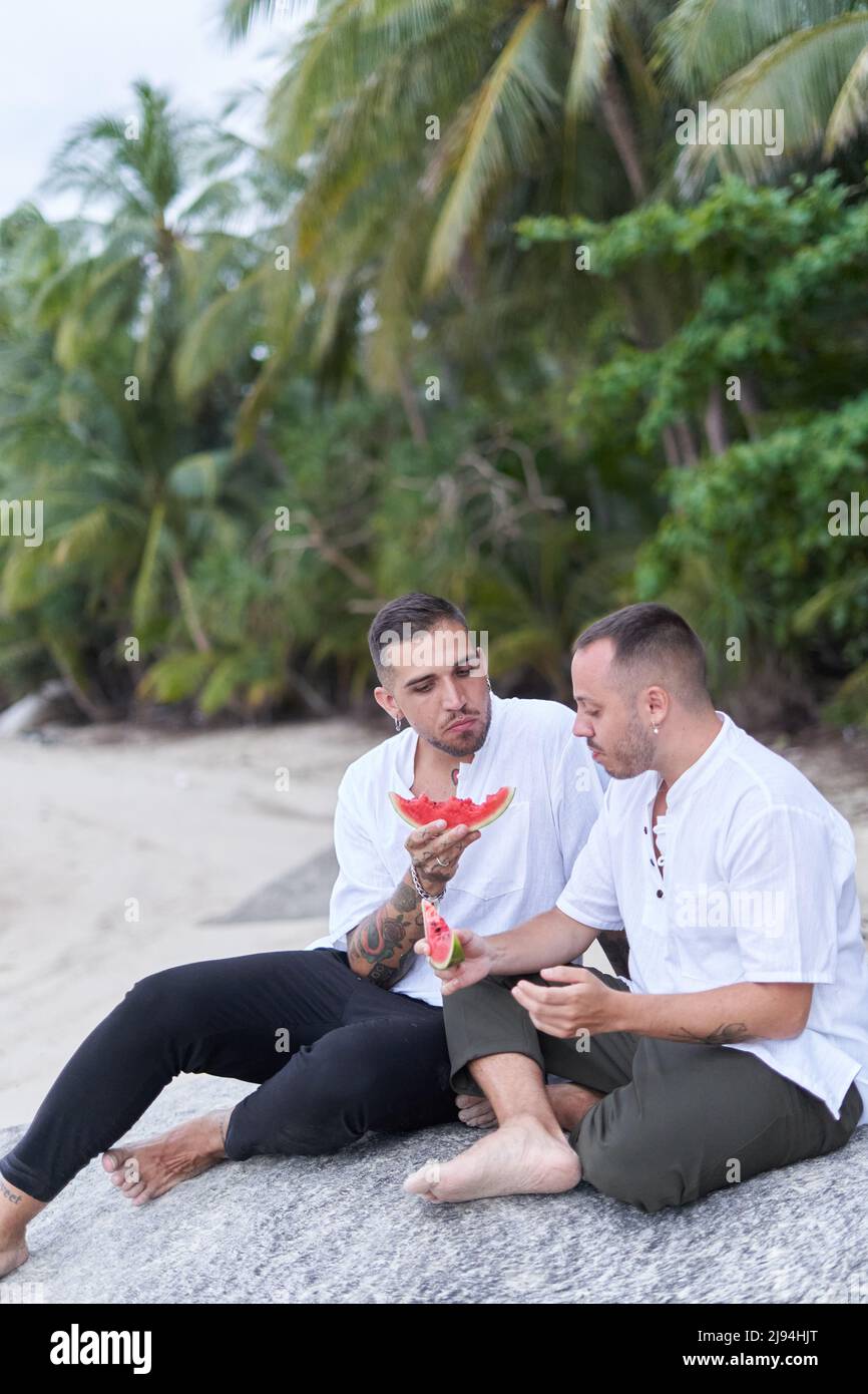 Foto verticale di una coppia gay che mangia il cocomero su una spiaggia Foto Stock