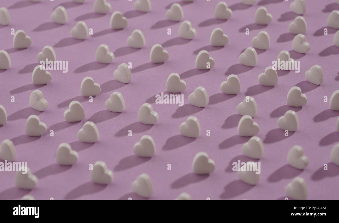 Modello senza cuciture di pillole bianche a forma di cuore su sfondo viola Foto Stock