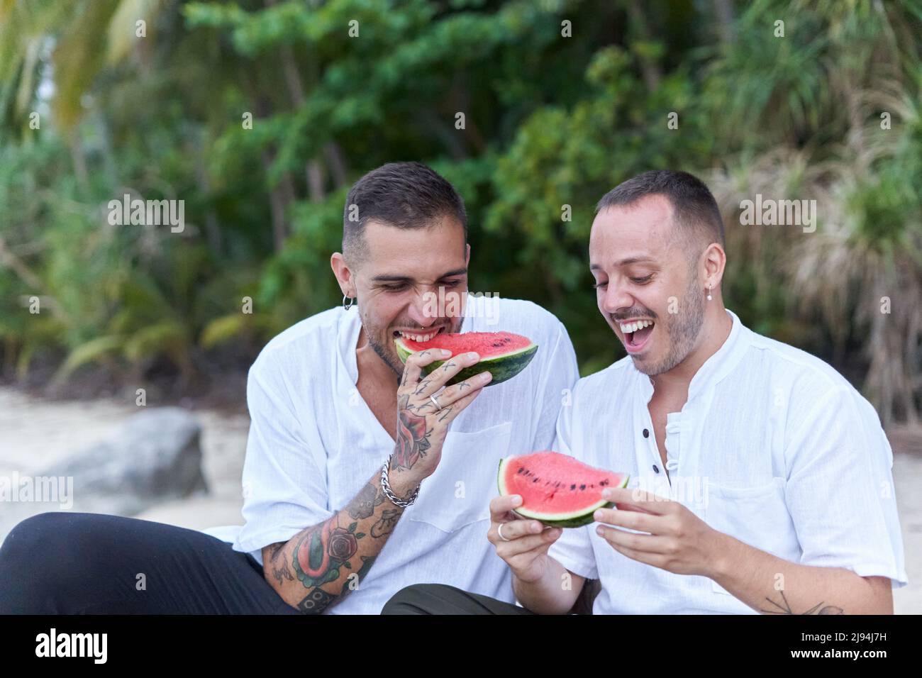 Sorridente coppia gay mangiare cocomero e chiacchierare rilassato all'aperto Foto Stock