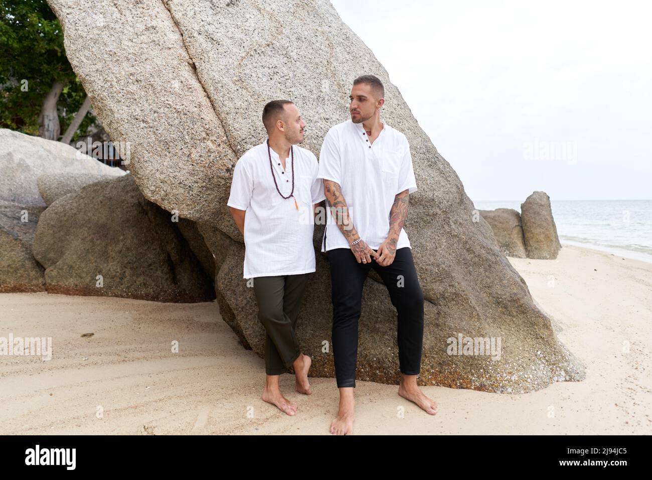 Coppia gay in piedi su una spiaggia vestita con abiti casual bianchi e neri Foto Stock