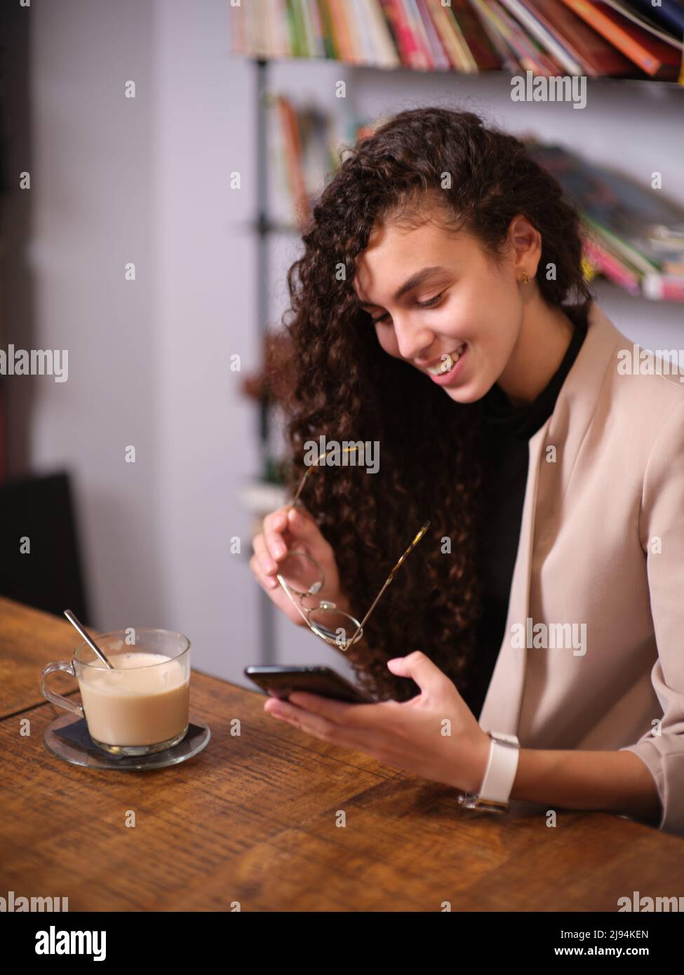 donna adulta che indossa i suoi bicchieri per guardare un messaggio telefonico, seduto con un drink in un bar Foto Stock