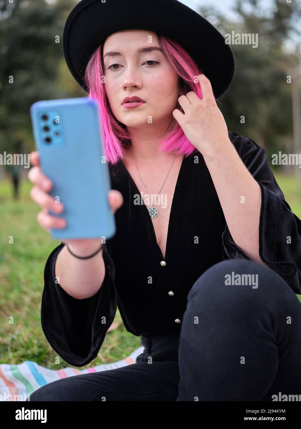donna in posa mentre guarda il suo cellulare e tocca i suoi capelli rosa Foto Stock