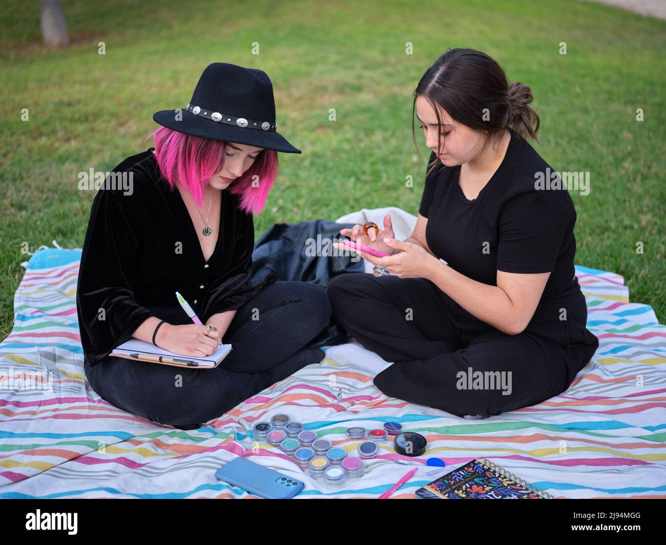 due ragazze che siedono su una coperta nel parco che progetta il make-up Foto Stock