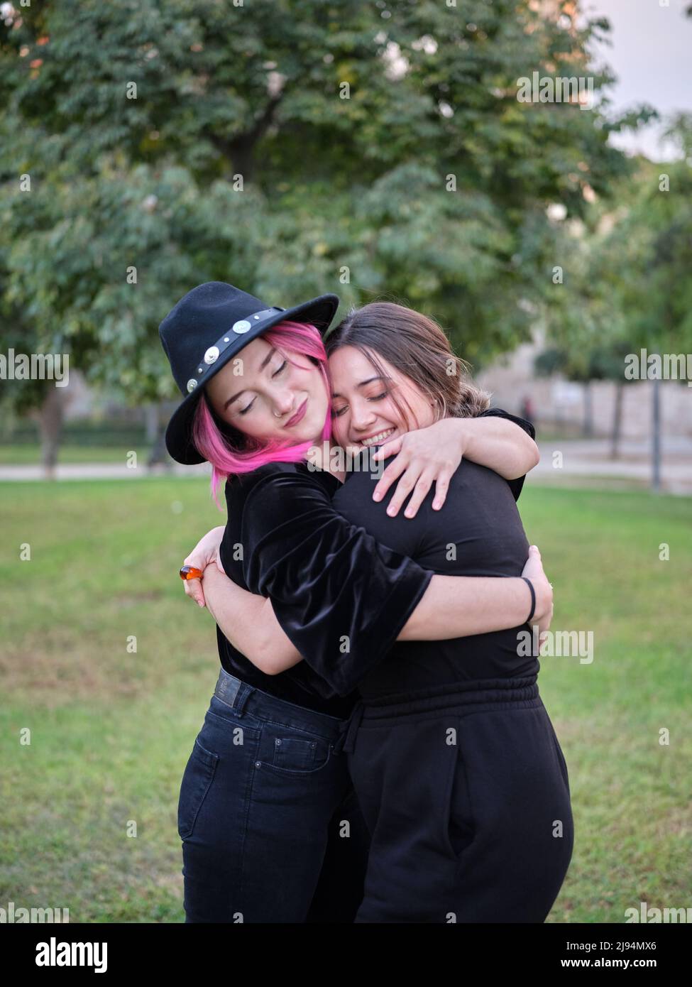 due amici in abiti neri che si abbraccia in piedi nel parco Foto Stock