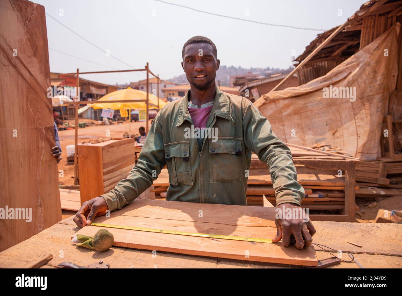 Carpentiere in un villaggio africano che prende le misure per fare un pezzo di mobili. Foto Stock