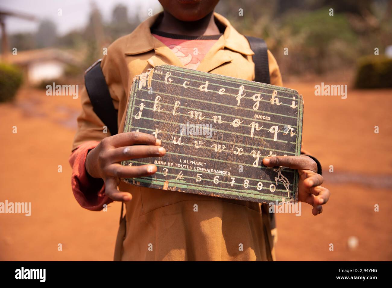 Il bambino africano mostra la sua lavagna con l'alfabeto e i numeri incisi su di esso. Concetto educativo. Foto Stock