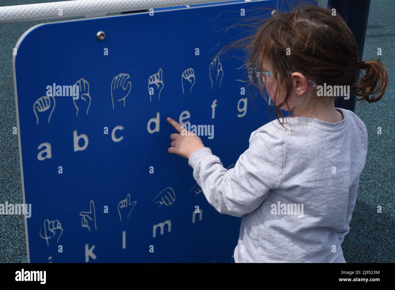 Una giovane ragazza guarda un grafico di linguaggio dei segni in un parco giochi a Edmonton, Alberta, Canada Foto Stock