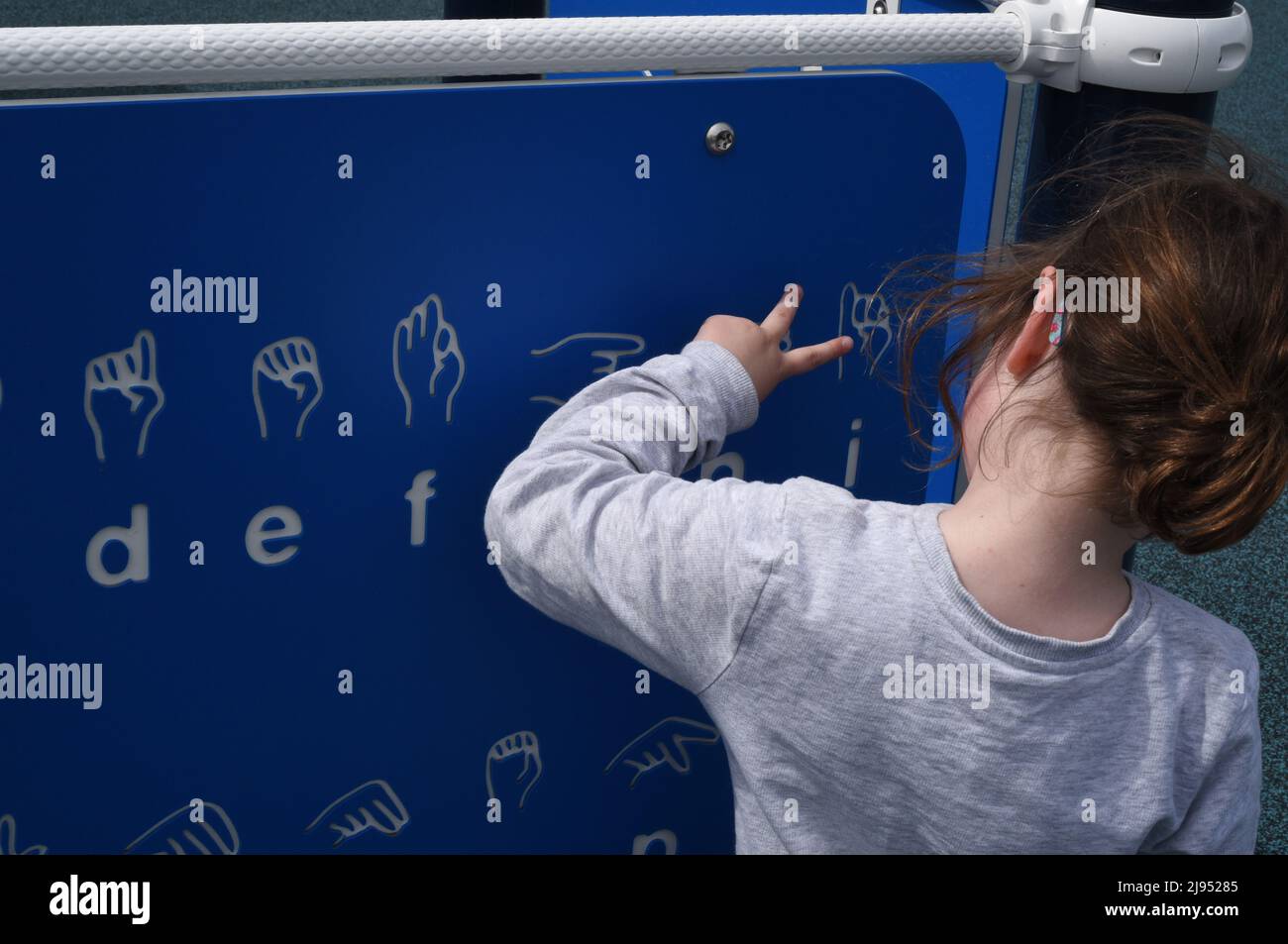 Una giovane ragazza guarda un grafico di linguaggio dei segni in un parco giochi a Edmonton, Alberta, Canada Foto Stock